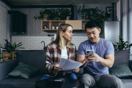 woman holding papers sitting on a coach with a man apply for a cash advance on his phone